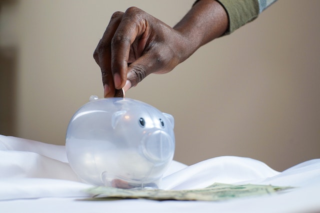 hand placing coins into a clear piggy bank